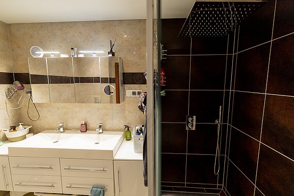 Modernes Badezimmer in Nord-Norwegen, mit Doppelwaschbecken, beleuchtetem Spiegel und dunkler Fliesendusche. Ideal für erholsamen Angelurlaub. Hochwertige Ausstattung sorgt für Komfort nach einem langen Tag am Wasser.