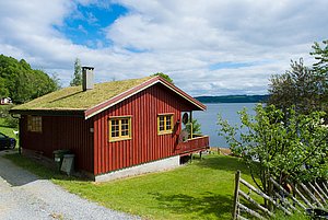 Rotes Haus mit Grasdach in der Region Hitra, Norwegen. Malerischer Blick auf den Fjord, umgeben von grüner Natur. Perfekt für Angelurlaub und Erholung. Entdecke die Schönheit Norwegens in Deinem nächsten Angelabenteuer!