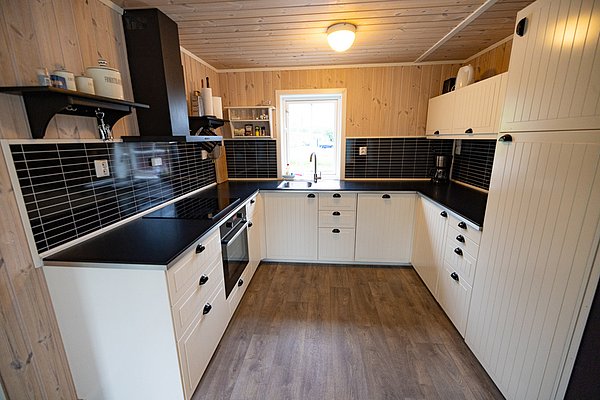 Gemütliche norwegische Ferienhausküche in Nordland: moderne Ausstattung, helle Holzverkleidung, schwarz-weiße Kontraste, Fenster mit natürlichem Licht. Ideal für erholsame Angelreisende.