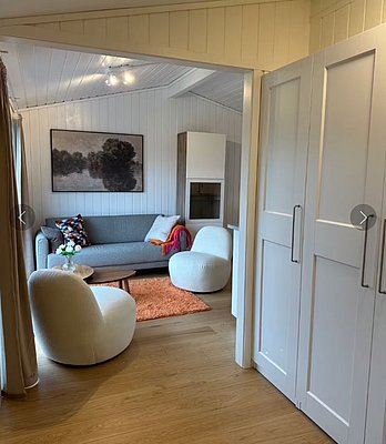 Gemütliches Wohnzimmer in einer Ferienhütte in Hitra, Norwegen. Modernes Sofa, weiße Sessel, Holzboden und Kunst an der Wand schaffen eine einladende Atmosphäre für entspannte Abende nach einem erfolgreichen Angeltag.