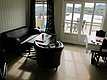 Gemütliches Wohnzimmer in Nordland, Norwegen, mit Ledersofas, Tisch und Stühlen vor großen Fenstern. Heller Holzboden mit Terrasse und Blick auf Fjordlandschaft. Perfekt für Entspannung nach einem erfolgreichen Angeltag.