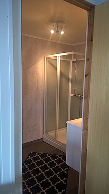 Helles Badezimmer in Nord-Norwegen mit moderner Duschkabine, schlichtem Teppich und eleganter Beleuchtung. Ideal für Angelreisen mit Komfort, Entspannung nach einem erfolgreichen Angelausflug garantiert. Perfekter Rückzugsort in der Natur.