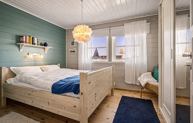 Gemütliches Schlafzimmer in Südwest-Norwegen mit Holzbett, blauer Akzentwand und skandinavischem Design. Helle Fenster mit zarten Vorhängen, Bücherregal und stimmungsvolle Beleuchtung schaffen eine einladende Atmosphäre für erholsame Angelurlaub-Nächte.