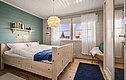 Gemütliches Schlafzimmer in Südwest-Norwegen mit Holzbett, blauer Akzentwand und skandinavischem Design. Helle Fenster mit zarten Vorhängen, Bücherregal und stimmungsvolle Beleuchtung schaffen eine einladende Atmosphäre für erholsame Angelurlaub-Nächte.