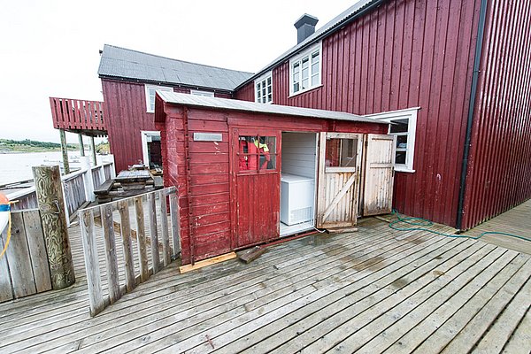 Rotes Holzgebäude in Nordland, Norwegen, direkt am Wasser. Skandinavische Architektur auf hölzernem Steg. Perfekt für Angelurlaube, um die idyllische Küstenlandschaft zu erleben. Entdecke fischreiche Gewässer in traumhafter Umgebung.