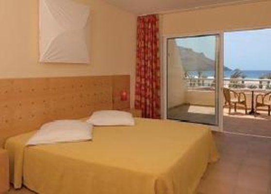 Ein Hotelzimmer mit einem Doppelbett, das gelbe Bettwäsche hat, neben einem Balkon mit Meerblick und Tisch mit Stühlen. Ein Hotelzimmer mit einem Doppelbett, das gelbe Bettwäsche hat, neben einem Balkon mit Meerblick und Tisch mit Stühlen.