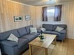 Gemütliches Wohnzimmer in Nord-Norwegen mit Holzwänden, grauen Sofas und dekorativen Kissen. Ein Holztisch mit Blumenarrangement schafft eine einladende Atmosphäre. Perfekte Unterkunft für erholsamen Angelurlaub in skandinavischer Natur.