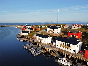 Küstenblick in Nordland, Norwegen: Malerisches Fischerdorf mit bunten Häusern und Booten am klaren Fjord, umgeben von beeindruckenden Berglandschaften. Perfekt für Angelreisen und Naturerlebnisse.
