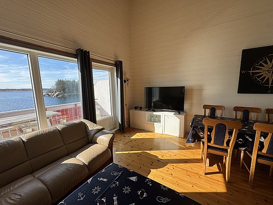 Gemütliches Wohnzimmer mit Holzfußboden in einem Ferienhaus auf Hitra, Norwegen. Panoramafenster bieten Blick auf die Küste und das Meer. Ideal für Angelurlaube in entspannter Atmosphäre. Perfekte Mischung aus Komfort und Natur.