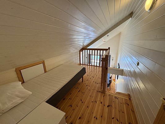 Gemütliches Loft-Zimmer in Hitra, Norwegen, mit Holzverkleidung und Einzelbett. Ideal für Angelurlaube, bietet es eine warme Atmosphäre und perfekten Rückzugsort nach einem erfolgreichen Angeltag. Verlockend für Abenteuerlustige und Ruhesuchende.
