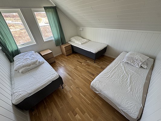 Helles Schlafzimmer in Hitra, Norwegen, mit zwei Einzelbetten, Holzfußboden und großen Fenstern. Ideal für erholsame Angelurlaube in Skandinavien. Entspannen nach erfolgreichen Angeltagen in komfortabler Unterkunft.