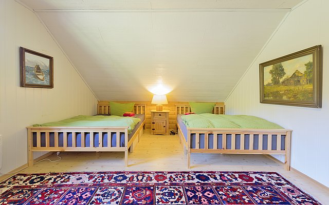 Gemütliches Schlafzimmer in Nordland, Norwegen: Zwei Betten mit grüner Bettwäsche, warmes Licht, bunte Teppiche. Perfekt für erholsamen Urlaub nach einem erfolgreichen Angeltag in der malerischen norwegischen Natur.