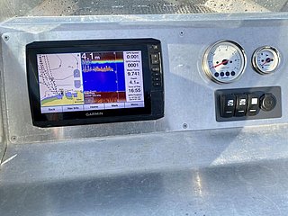 Das Bild zeigt ein Bootspanel mit einem Garmin-Echolot-Display, das Wassertiefe und Temperatur anzeigt, sowie analoge Anzeigen und Schalter.