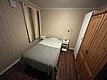 Gemütliches Schlafzimmer in Südwest-Norwegen: Holzwände und Holzboden, Einzelbett mit grauer Decke, zwei Nachttische, Leselampe, Kleiderschrank. Ideal für ruhige Nächte nach erfolgreichen Angelabenteuern. Perfekte Unterkunft für jeden Angelurlaub.
