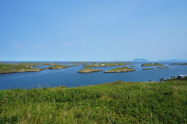 Weite Landschaft Nordlands in Norwegen: Grüne Hügel, glitzernde Seen, zerstreute Inseln, unter wolkenlosem, blauem Himmel. Perfekt für ruhigen Angelurlaub und unvergessliches Naturerlebnis. Ideal zum Entspannen und Fische fangen.