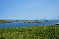 Weite Landschaft Nordlands in Norwegen: Grüne Hügel, glitzernde Seen, zerstreute Inseln, unter wolkenlosem, blauem Himmel. Perfekt für ruhigen Angelurlaub und unvergessliches Naturerlebnis. Ideal zum Entspannen und Fische fangen.