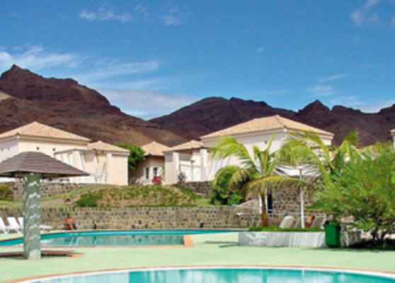 Ein tropischer Ferienort mit zwei Swimmingpools, Palmen und weißen Gebäuden vor einer Bergkulisse unter klarem blauem Himmel. Ein tropischer Ferienort mit zwei Swimmingpools, Palmen und weißen Gebäuden vor einer Bergkulisse unter klarem blauem Himmel.