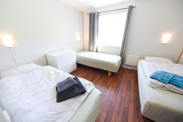 Gemütliches Schlafzimmer in Hitra, Norwegen, mit drei Einzelbetten und heller Einrichtung. Perfekt für Angler, die nach einem ereignisreichen Tag in ruhiger Umgebung entspannen möchten. Ideal für Angelreisen in Norwegen.