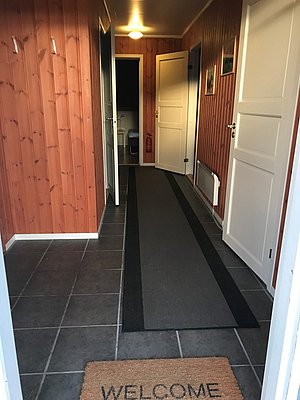 Gemütlicher Eingangsbereich einer Angelhütte in Hitra, Norwegen, mit Holzwänden und Willkommensmatte. Ideal für Angelurlaub und Abenteuer in der skandinavischen Natur. Perfekt zum Entspannen nach erfolgreichen Angelstunden.