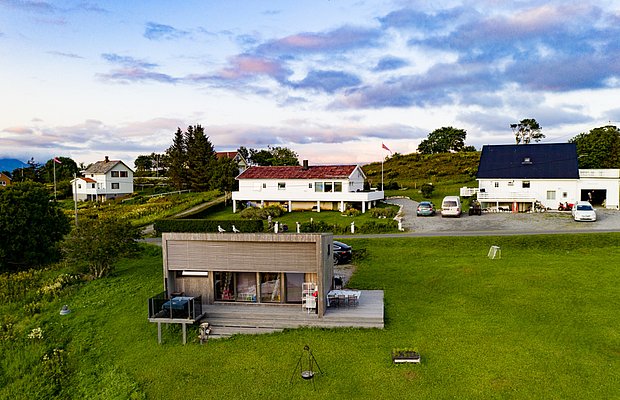 Kleines, modernes Ferienhaus in Norwegen, umgeben von üppigem Grün und traditionellen Gebäuden. Ideal für einen entspannten Angelurlaub in Nordland. Die Landschaft bietet Ruhe und atemberaubende Ausblicke, perfekt für Erholungssuchende.