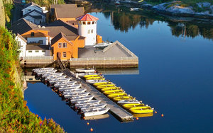 Ruhiger Hafen in Südwest-Norwegen mit Bootssteg, weißen und gelben Booten vor malerischer Kulisse. Die farbenfrohen Gebäude spiegeln sich im stillen Wasser und versprechen ein idyllisches Angelabenteuer. Perfekter Startpunkt für Angelreisen in Norwegen.