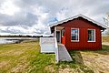 Gemütliches rotes Ferienhaus in Hitra, Norwegen. Die Hütte steht direkt am Wasser und bietet idyllische Ausblicke, perfekt für Angelurlaub. Umgeben von grüner Wiese und Wolkenhimmel, idealer Ausgangspunkt für Entdecker und Angler.