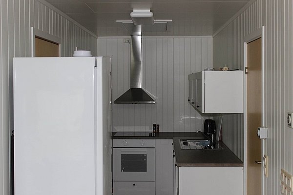 Moderne, helle Küche in Nord-Norwegen mit weißen Wänden, Kühlschrank, Herd, Dunstabzugshaube und Spüle. Ideal für Angelreisende, die kulinarische Abende in gemütlicher Unterkunft genießen möchten. Perfekt für entspanntes und komfortables Kochen nach einem erfolgreichen Angelausflug.