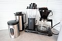 Auf einer modernen Küchenarbeitsplatte stehen eine Moccamaster Kaffeemaschine, eine Isolierkanne und ein Kaffeebehälter aus Edelstahl.