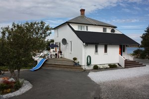 Weißes Holzhaus in Hitra, Norwegen, mit Terrasse, blauer Rutsche und Meerblick. Ideal für Angelreisen und Erholung. Umgeben von grüner Natur, bietet es entspannte Urlaubsatmosphäre nahe der norwegischen Küste. Perfekt für Abenteuer und Entspannung.