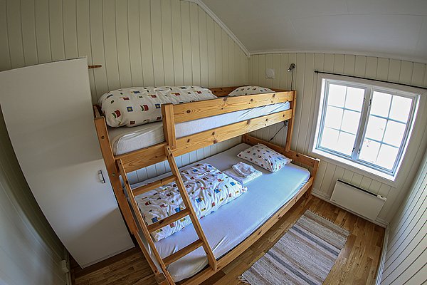 Gemütliches Schlafzimmer in Nord-Norwegen: Etagenbett aus Holz, schlichte Einrichtung, helle Wände, Fenster mit Tageslicht. Ideal für Angelurlaub. Perfekt zum Entspannen nach einem erfolgreichen Angeltag in der beeindruckenden nordischen Natur.