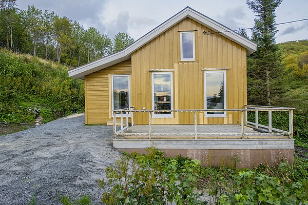 Gelbes Holzhaus in Nordland, Norwegen, umgeben von grüner Landschaft. Perfekt für entspannende Angelurlaube in der Natur, bietet das Haus eine idyllische Kulisse für Outdoor-Abenteuer und entspannte Momente.