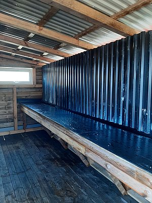 Innenansicht eines hölzernen Schuppens mit Wellblechdach in Hitra, Norwegen. Holzstruktur und Fenster sorgen für rustikalen Charme und Atmosphäre – idealer Ausgangspunkt für Angelreisen und Abenteuer in der Region.