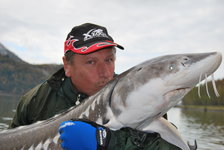 Ein Angler hält einen großen Stör in den Armen, während er beim Angeln im Freien posiert.