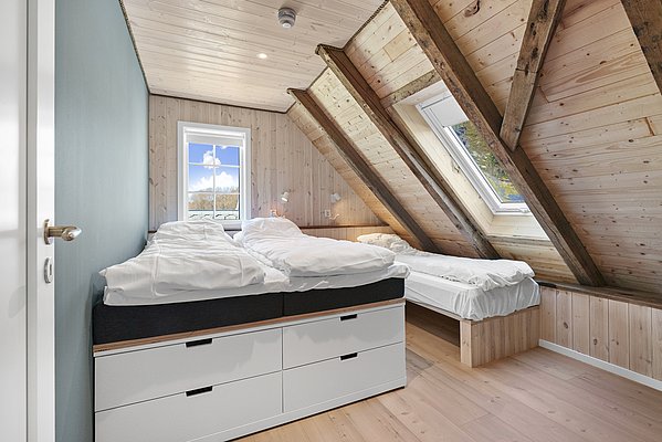 Gemütliches Schlafzimmer in Südwest-Norwegen mit Holzwänden, zwei Einzelbetten unter Dachschrägen. Helles Tageslicht durch Fenster, beruhigende Atmosphäre. Ideal für erholsame Nächte nach einem erfolgreichen Angeltag in Norwegen.