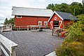 Rote Holzgebäude am Wasser auf Hitra, Norwegen. Idyllisch, mit großem Holzdeck und umgeben von grüner Natur. Perfekter Ausgangspunkt für Angelreisen und Meeresangeln in skandinavischer Landschaft.