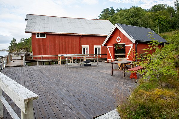 Rote Holzgebäude am Wasser auf Hitra, Norwegen. Idyllisch, mit großem Holzdeck und umgeben von grüner Natur. Perfekter Ausgangspunkt für Angelreisen und Meeresangeln in skandinavischer Landschaft.