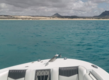 Blick von einem Boot auf das türkisfarbene Meer vor der Küste von São Vicente, Kapverden. Sandige Strände und bergige Landschaft im Hintergrund unter bewölktem Himmel. Perfekt für Angelreisen und Meeresabenteuer.