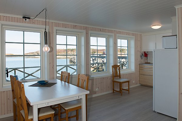 Ein heller, gemütlicher Raum mit Holzmöbeln und großen Fenstern bietet einen Ausblick auf ein ruhiges Gewässer und eine felsige Küste.