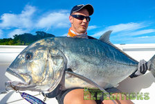 Ein Angler hält einen riesigen GT (Giant Trevally) auf einem Boot in Tansania, strahlend blauer Himmel. Perfekter Moment für Angelbegeisterte im Angelurlaub. Abenteuer und unvergessliche Fänge erwarten dich!