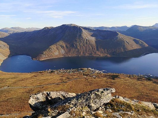 Panoramablick auf eine malerische Bucht in Nord-Norwegen mit umliegenden Bergen und einem idyllischen Dorf am Ufer, perfekter Ort für unvergessliche Angelreisen. Friedliche Landschaft ideal für Entspannung und Naturerleben.