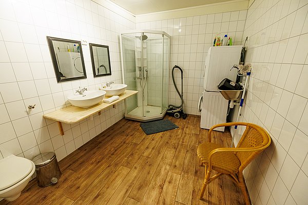 Geräumiges Badezimmer in Nordland, Norwegen, mit moderner Dusche, zwei Waschbecken und Waschmaschine. Die Holzböden sorgen für eine warme Atmosphäre. Ideal für Gäste, die Komfort und Funktionalität schätzen.