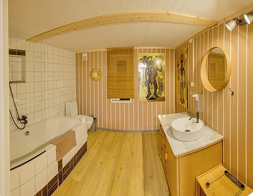 Gemütliches Badezimmer in Nordland, Norwegen: warme Holztöne, moderne Badewanne, runder Spiegel und dekorative Elemente. Perfekte Entspannungsoase nach erlebnisreichen Angelabenteuern. Ideal für Ihren nächsten Angelurlaub im hohen Norden.