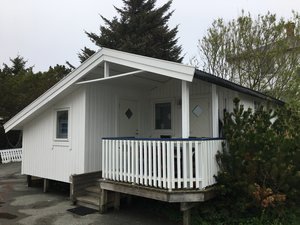Weißes Holzferienhaus in Hitra, Norwegen, umgeben von grünen Bäumen. Ideal für Angelurlaub, bietet gemütliche Unterkunft in natürlicher Umgebung. Perfekt für Erholung und Abenteuer beim Meeresangeln.