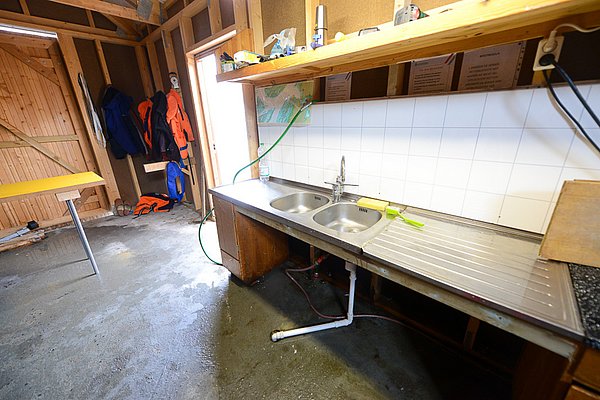 Angelhaus in Nordland, Norwegen: Einfache Fischverarbeitungsküche mit Doppeltspüle, Arbeitsfläche und Angelkleidung. Perfekt für Anglerurlaube in atemberaubender Umgebung. 

**Keywords:** Angelreisen, Nordland, Norwegen, Fischverarbeitungsküche.