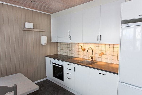 Moderne norwegische Küche mit weißen Schränken, Elektroherd und Spüle, ideal für Angelreisende in Nord-Norwegen. Helle Wanddekorationen und eine gemütliche Atmosphäre sorgen für Komfort nach einem erlebnisreichen Angeltag.