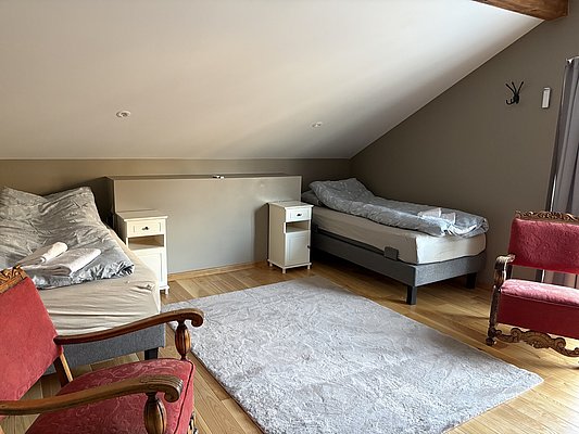 Gemütliches Schlafzimmer in Nord-Norwegen, hell, mit zwei Einzelbetten, Holzfußboden, Teppich, roten Sesseln und Nachttischen. Perfekt für entspannte Angelurlaube und Erholung nach einem erfolgreichen Tag am Wasser.