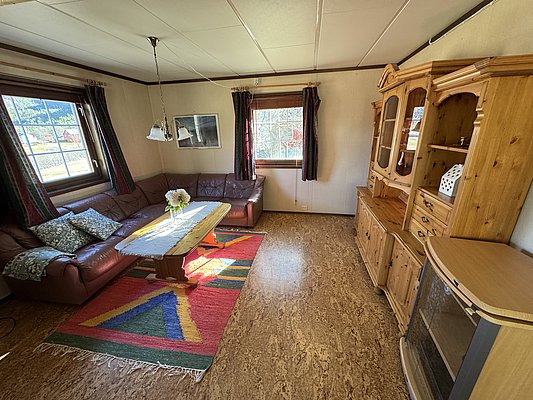 Gemütliches Wohnzimmer in Hitra, Norwegen: Ledersofa, Holztisch, bunte Teppiche und große Fenster mit Aussicht. Ideale Unterkunft für einen Angelurlaub in beeindruckender skandinavischer Umgebung. Entspannt nach einem erfolgreichen Angelausflug erholen.