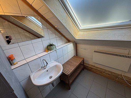 Helles Badezimmer mit Dachfenster in Hitra, Norwegen. Moderne weiße Fliesen, Waschbecken, Spiegel und Holzbank schaffen ein einladendes Ambiente. Ideal für eine entspannte Pause nach einem erfolgreichen Angelausflug.