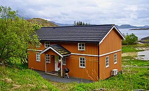 Oranges Holzhaus in Nordland, Norwegen, umgeben von grüner Natur und Blick auf das Meer. Perfekt für Angelreisen und Entspannung inmitten idyllischer skandinavischer Landschaft.