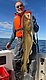 Ein Angler hält stolz einen großen Kabeljau an Bord eines Bootes vor der beeindruckenden Kulisse der Norwegischen See bei Hitra. Perfektes Angelabenteuer bei strahlendem Sonnenschein und klarem Himmel.